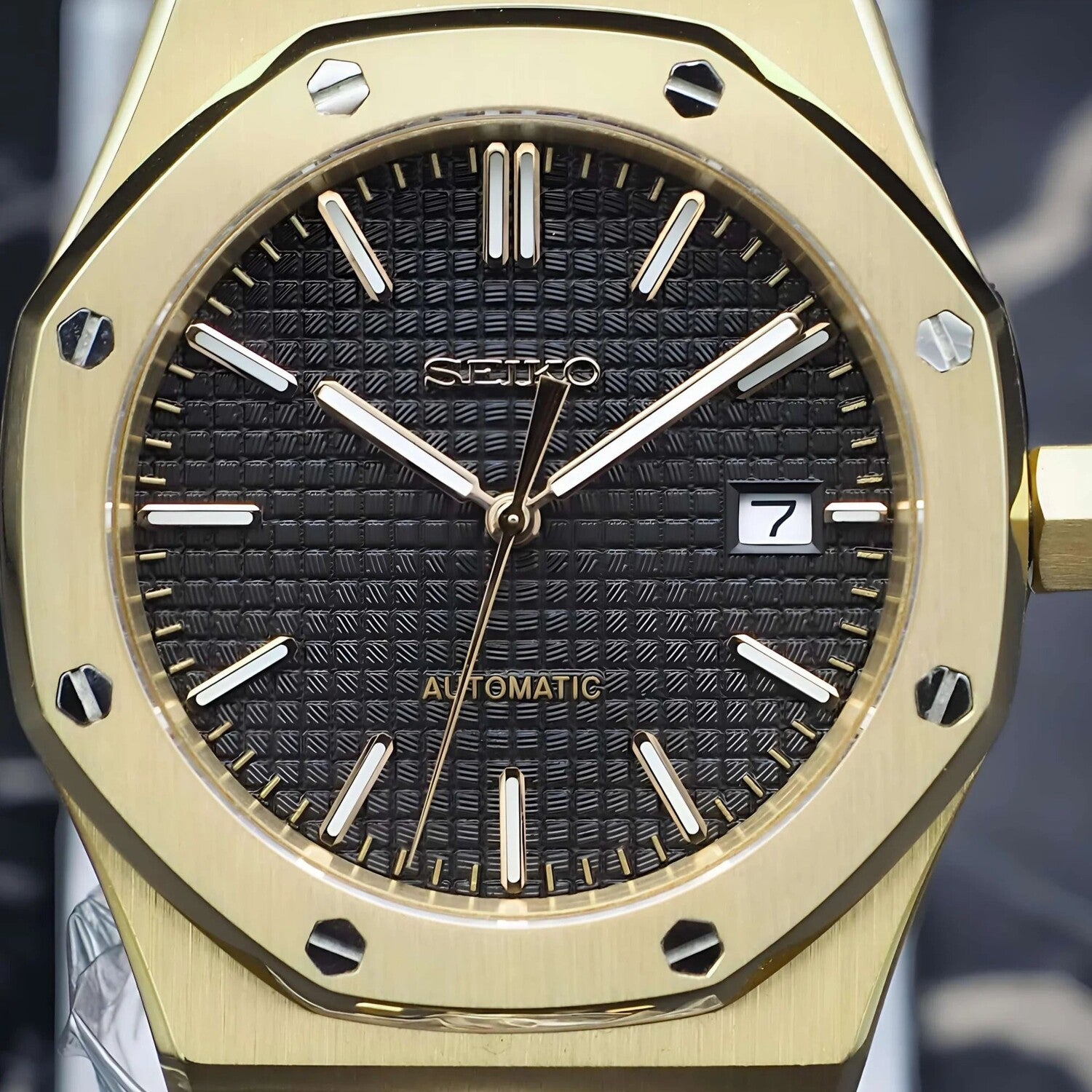 Close up of Seiko Mod Royal Oak in yellow gold, featuring a black textured dial with gold tone hands, baton markers, and a date display at three o’clock.