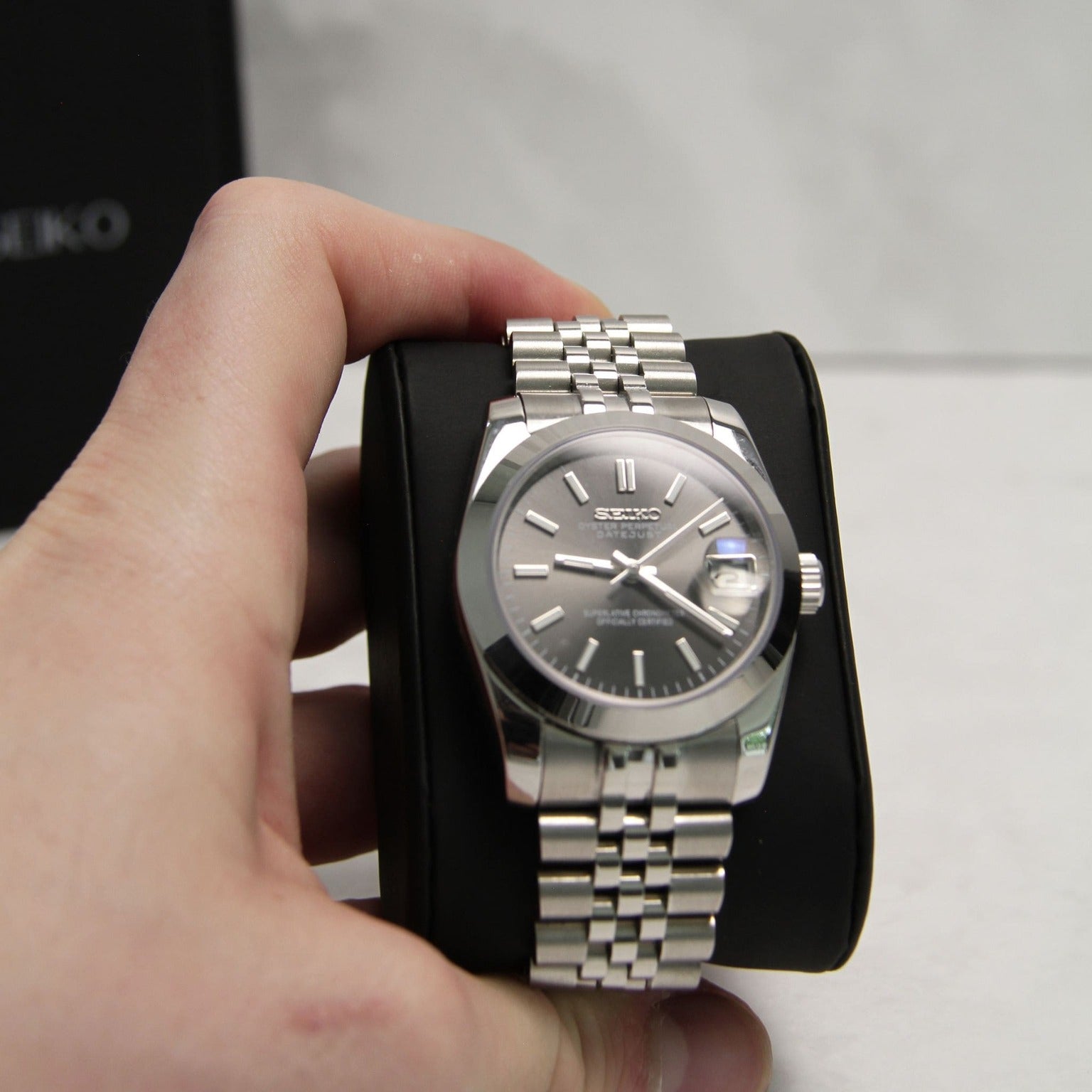 Seiko Mods Datejust Grey Smooth Bezel front view held in hand, bracelet resting on black cushion
