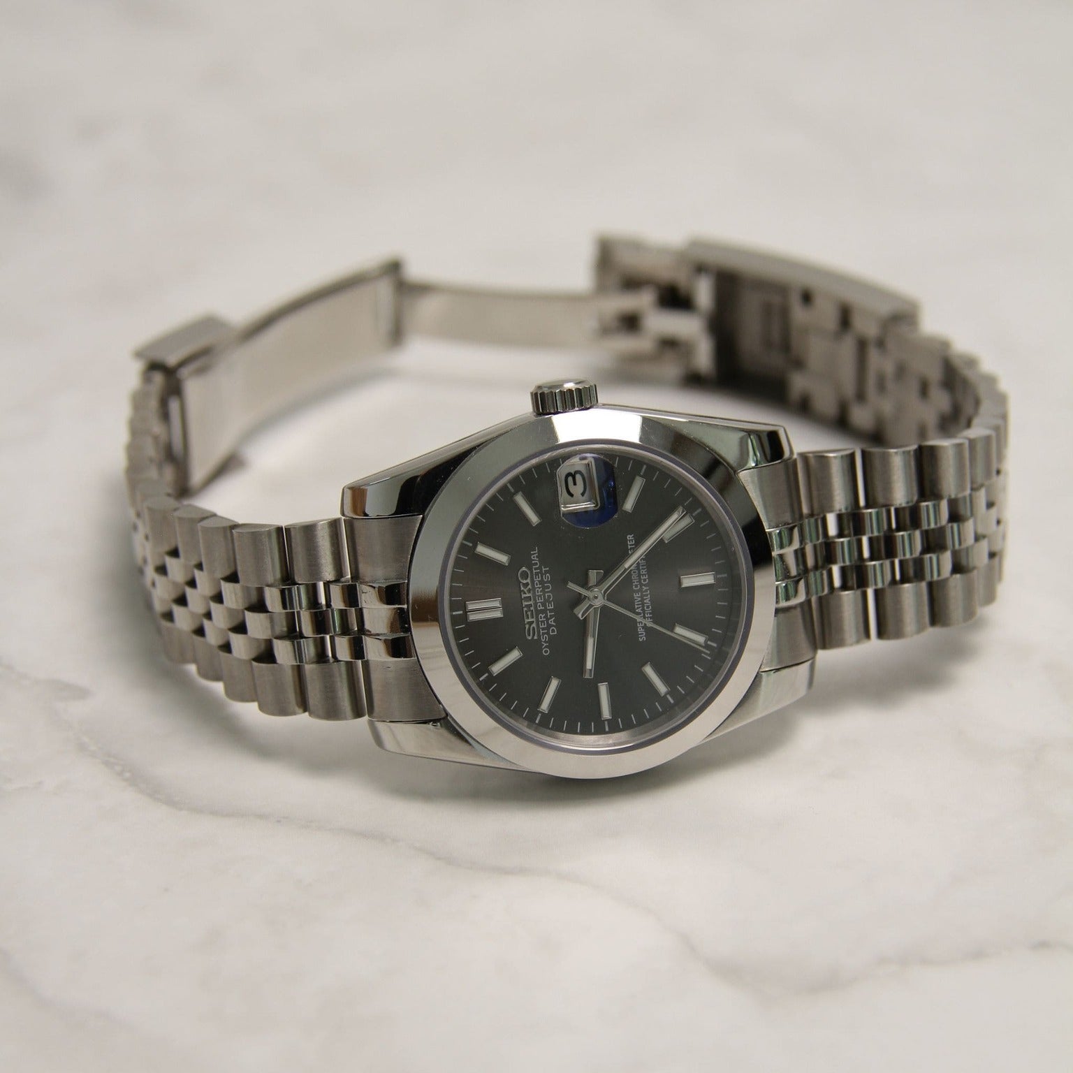 Seiko Mods Datejust Grey Smooth Bezel horizontal view on marble surface, open jubilee bracelet