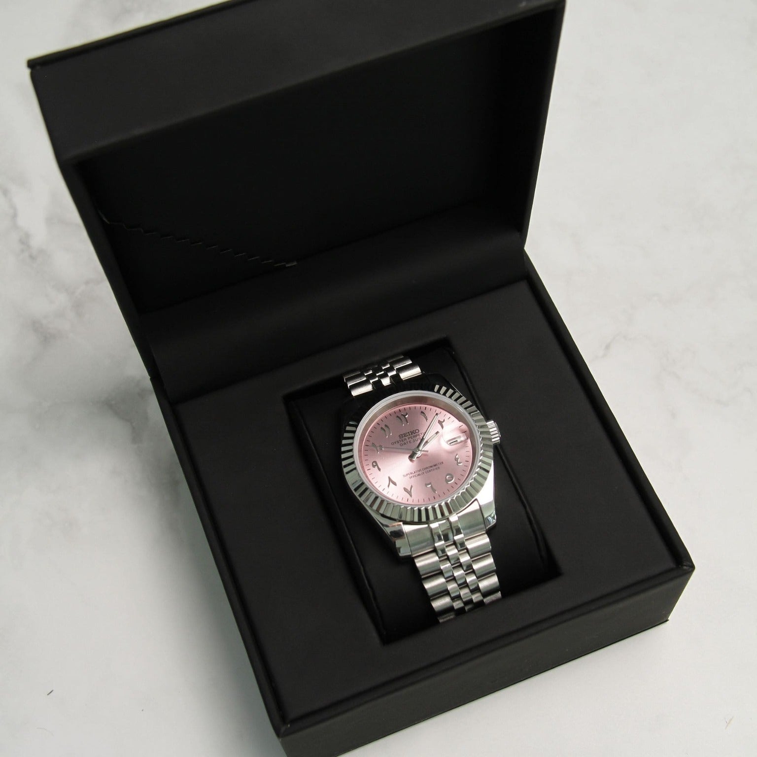 Seiko Mods Datejust Rose Arabic seen inside black presentation box on marble background