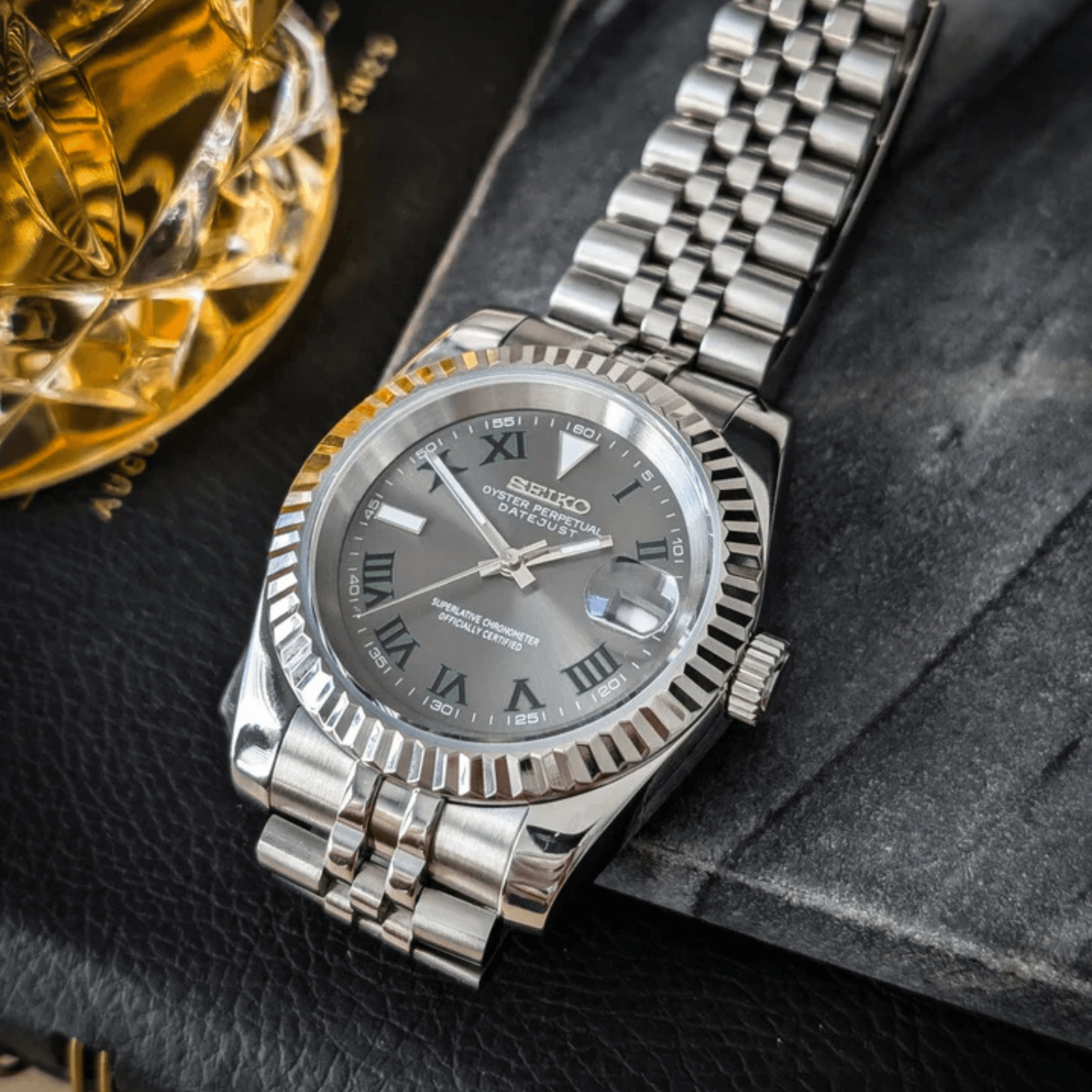 Right angled close up of Seiko Mod Datejust Wimbledon showing polished case and silver fluted bezel beside glass.