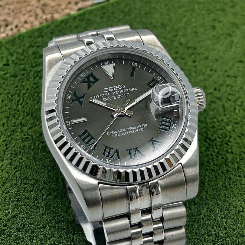 Front view of Seiko Mod Datejust Wimbledon with dark grey dial and green Roman numerals on grass background.