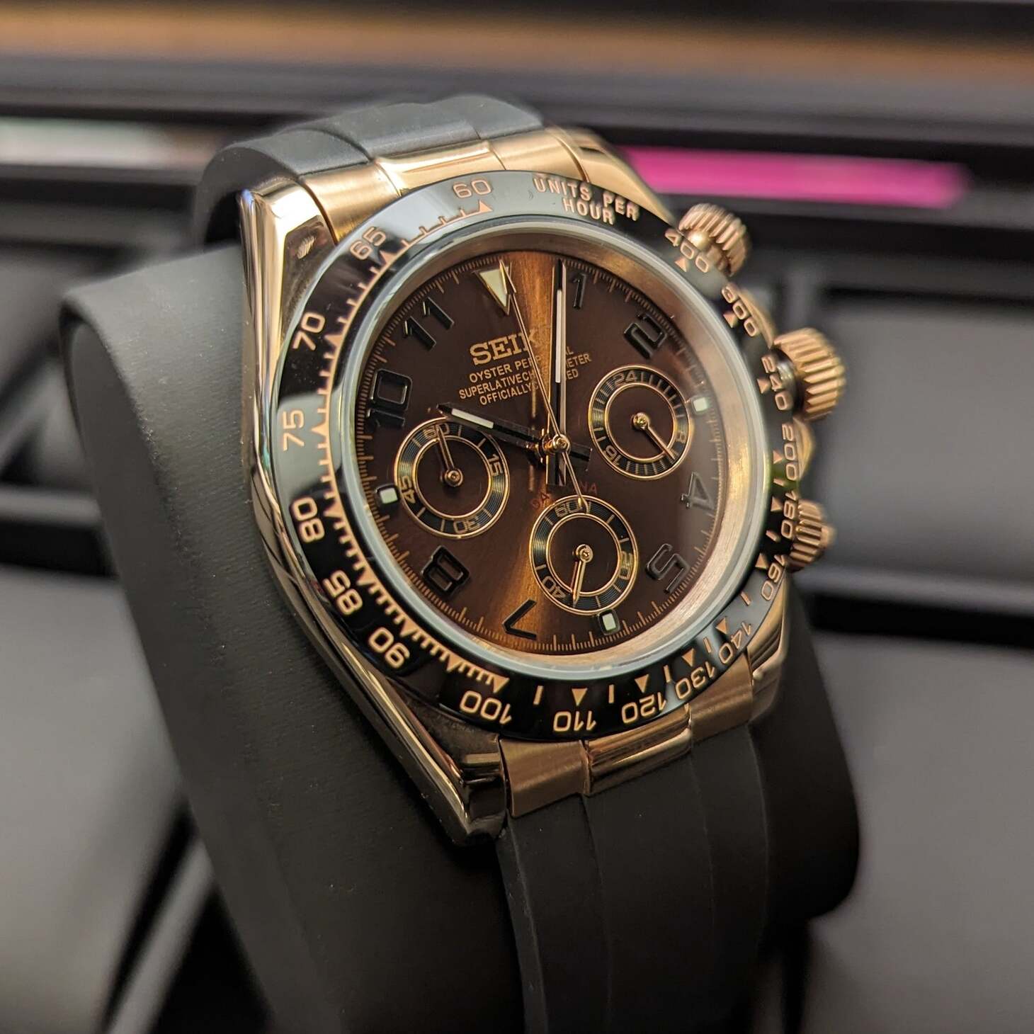 Left angled close up of a rose gold Seiko Mod Daytona with black ceramic tachymeter bezel, chocolate brown dial, luminous markers, and rubber strap.