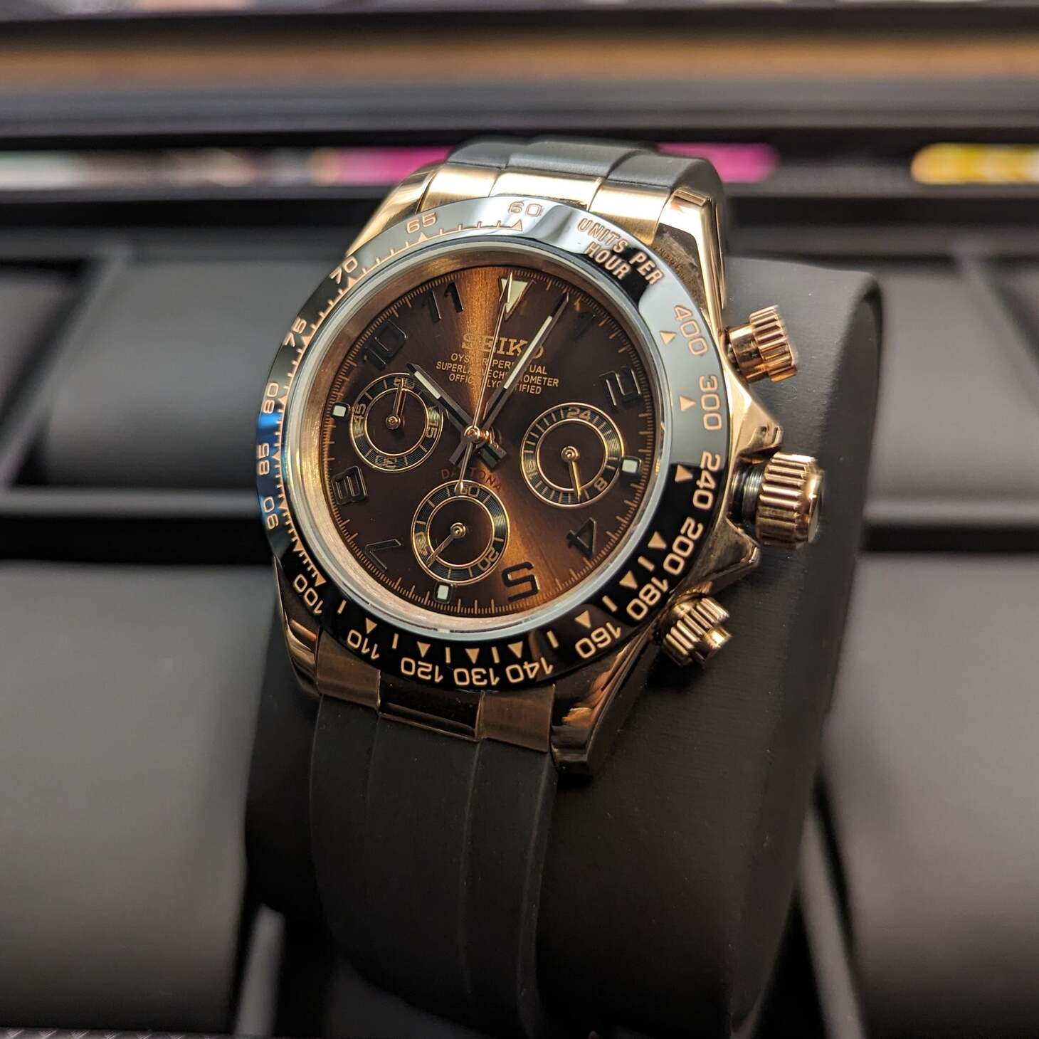 Right three quarter view of a rose gold Seiko Mod Daytona with sunburst chocolate dial, three chronograph subdials, and black rubber strap on display.