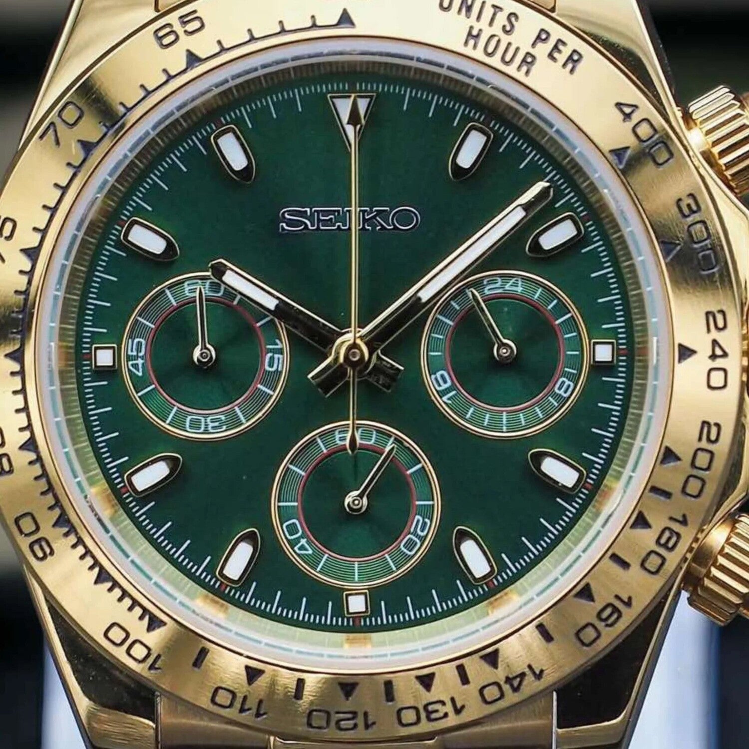 Close up of the Seiko Mod Daytona in gold focusing on the green dial with three detailed subdials, gold hands, and engraved tachymeter bezel.