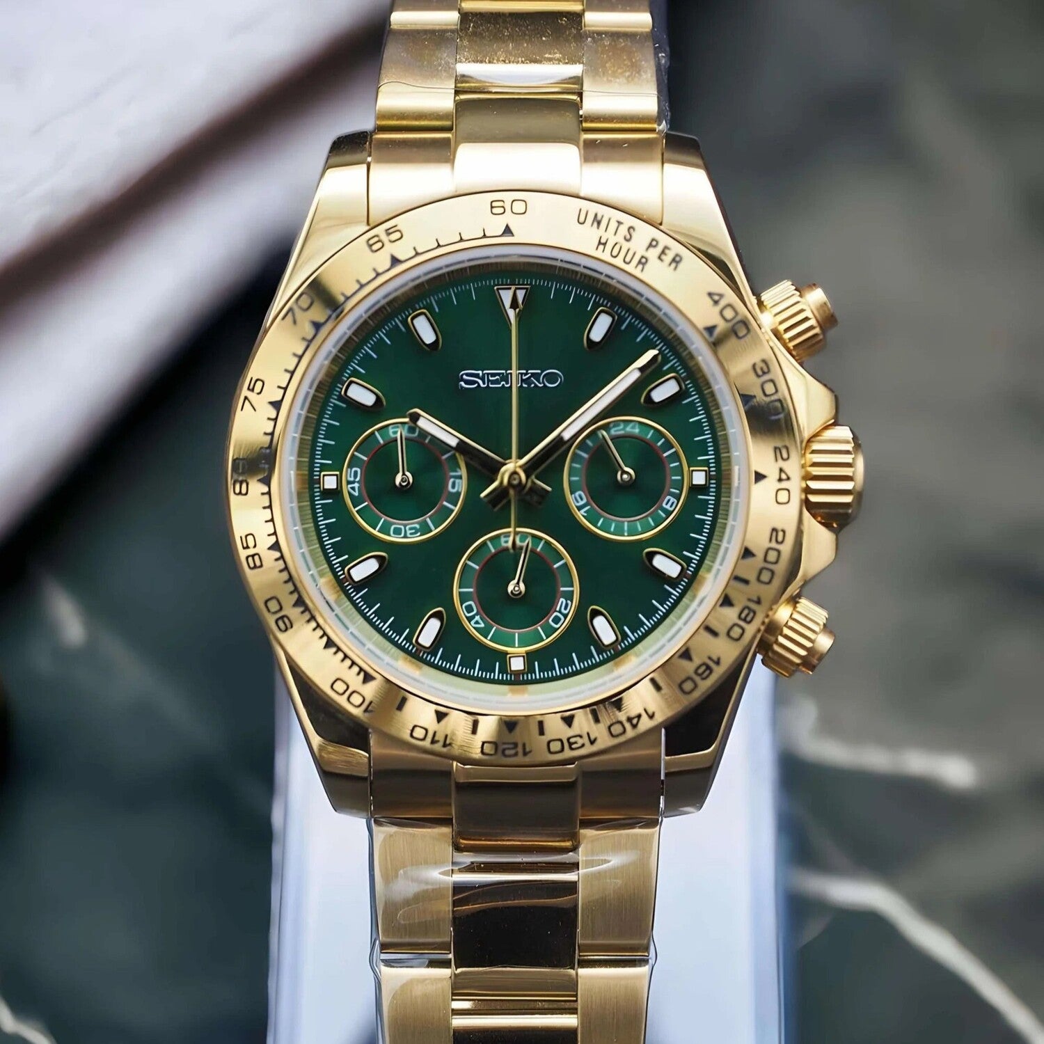 Front view of the Seiko Mod Daytona in yellow gold featuring a glossy green dial, three subdials with golden accents, and a polished oyster style bracelet.