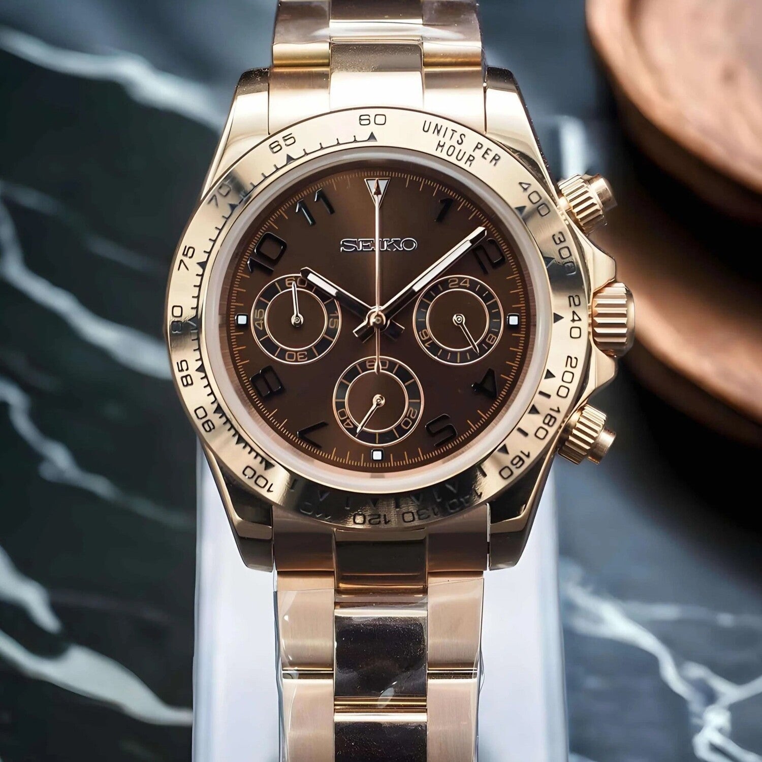 Front view of the Seiko Mod Daytona in rose gold with chocolate dial displayed on a marble-patterned background.