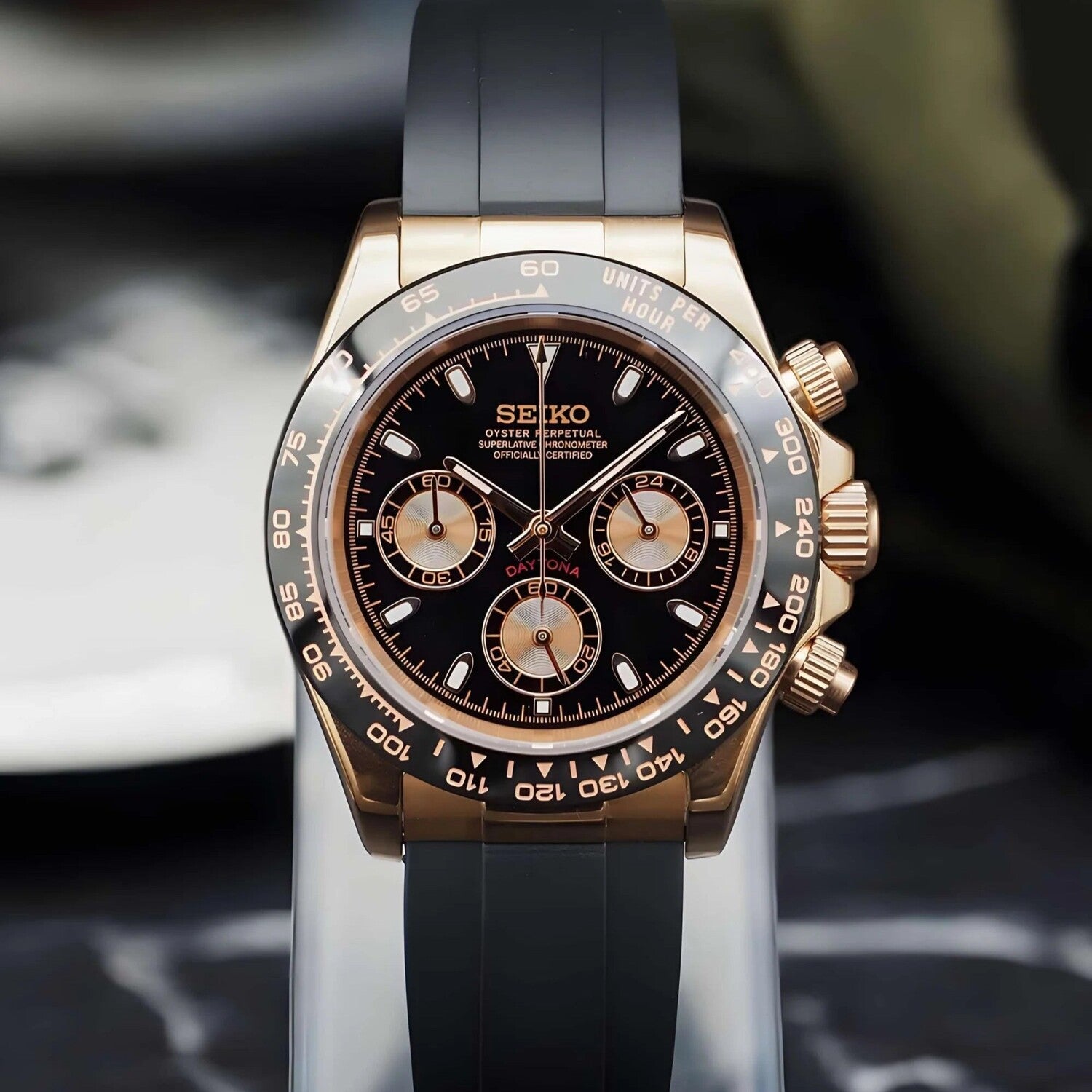 front view of the Seiko Mod Daytona in rose gold on a black rubber strap, showcasing its black dial and gold accents.