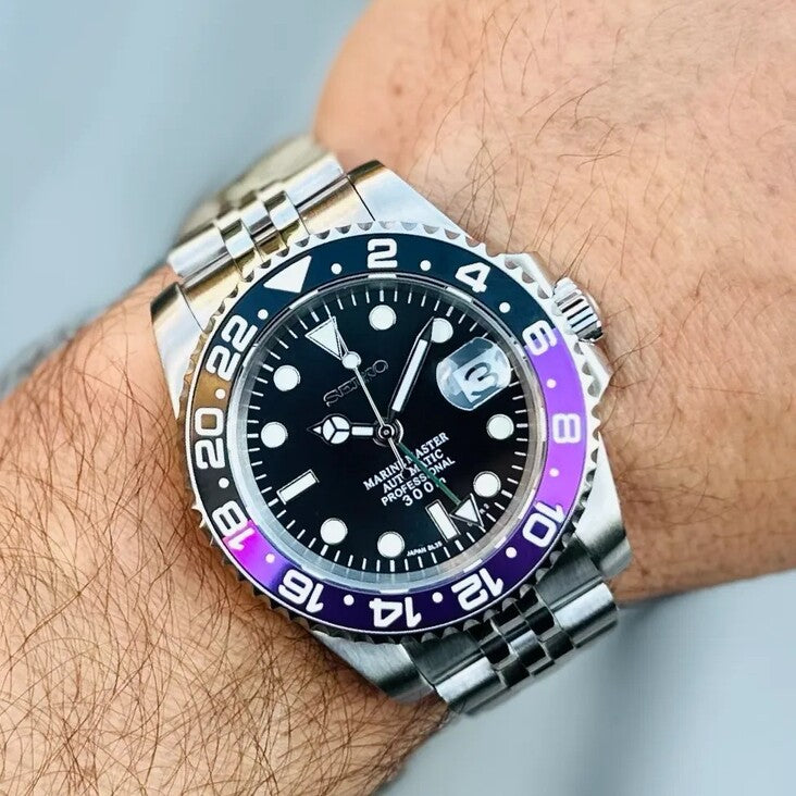 Wrist shot Seiko Mod GMT Joker displaying purple black bezel and brushed steel bracelet in natural light