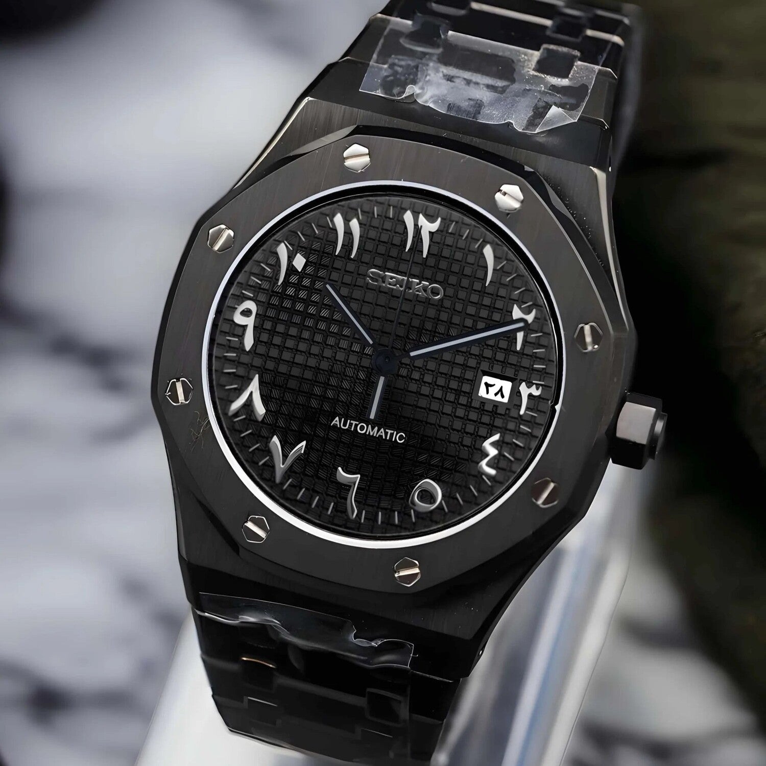 Left angled view of the Seiko Mod Royal Oak automatic watch with Arabic script dial, black waffle textured surface, brushed black stainless steel case, and integrated steel bracelet