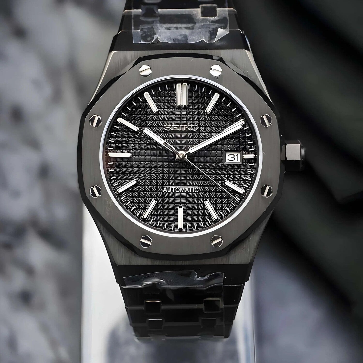 Front view of the Seiko Mod Royal Oak automatic watch in all black with a detailed waffle pattern dial, luminous silver indices, brushed stainless steel case, and matching black bracelet