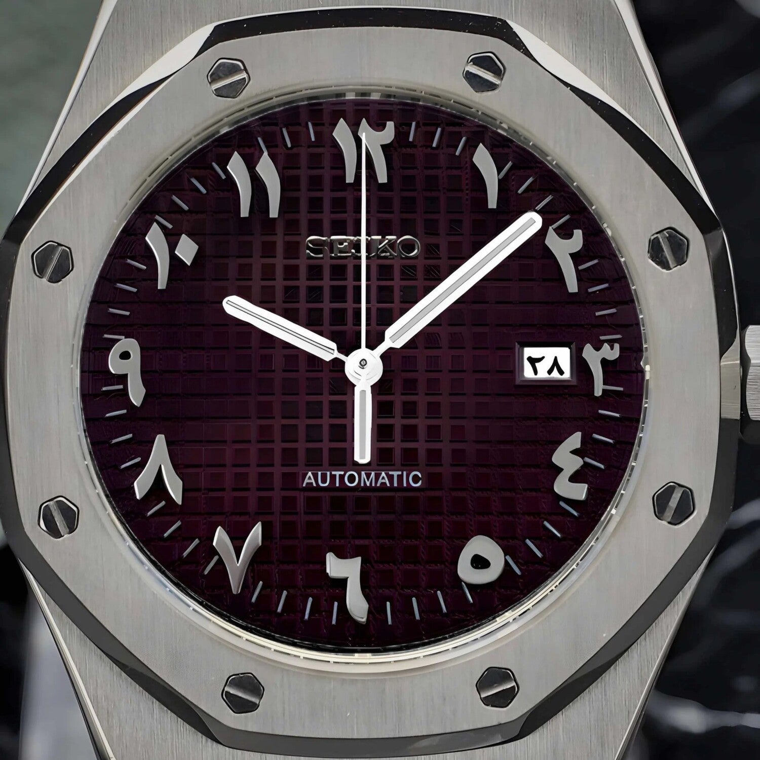 Close up of the Seiko Mod Royal Oak brown dial with Arabic numerals, silver hands, brushed octagonal bezel, and a framed date display
