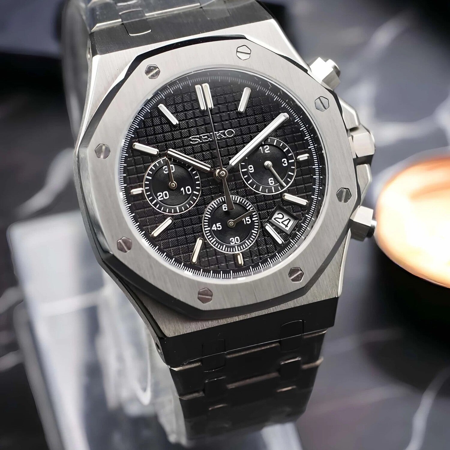Angled close up of the Seiko Mod Royal Oak VK63 chronograph watch with black waffle pattern dial, three subdials, brushed stainless steel case, and date at 10 o’clock