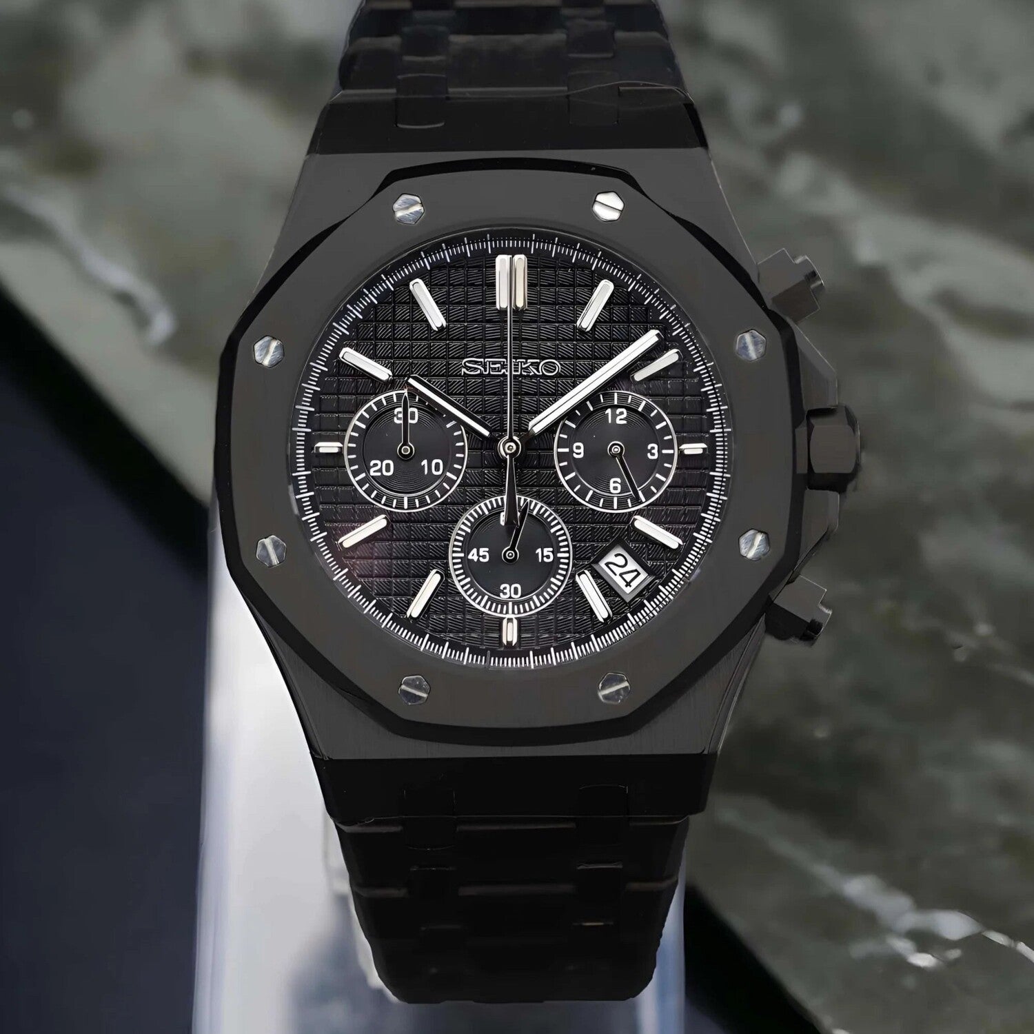 Front view of the Seiko Mod Royal Oak VK63 chronograph in an all black finish with a textured dial, three contrasting subdials, integrated black bracelet, and a small date aperture near 4 o’clock