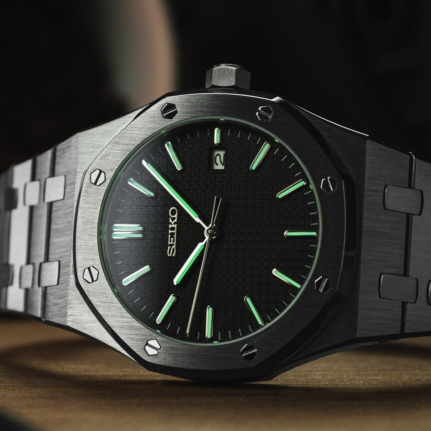 Angled close up of the Seiko Mod Royal Oak with black textured dial, featuring bright green luminous markers and brushed stainless steel case against a dark background.