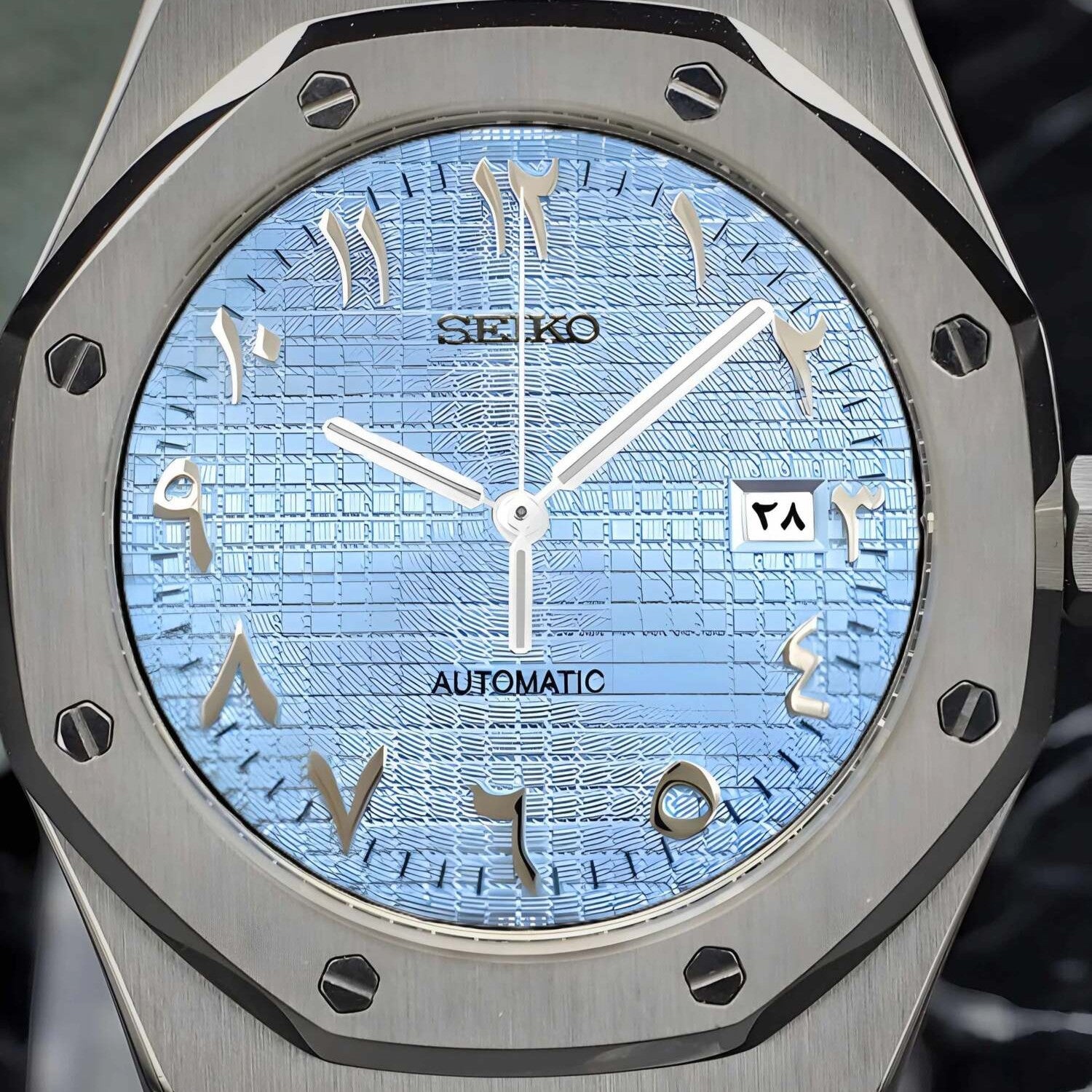 Close up of Seiko Mod Royal Oak with ice blue textured dial, Arabic numerals, brushed stainless steel bezel and visible date window.