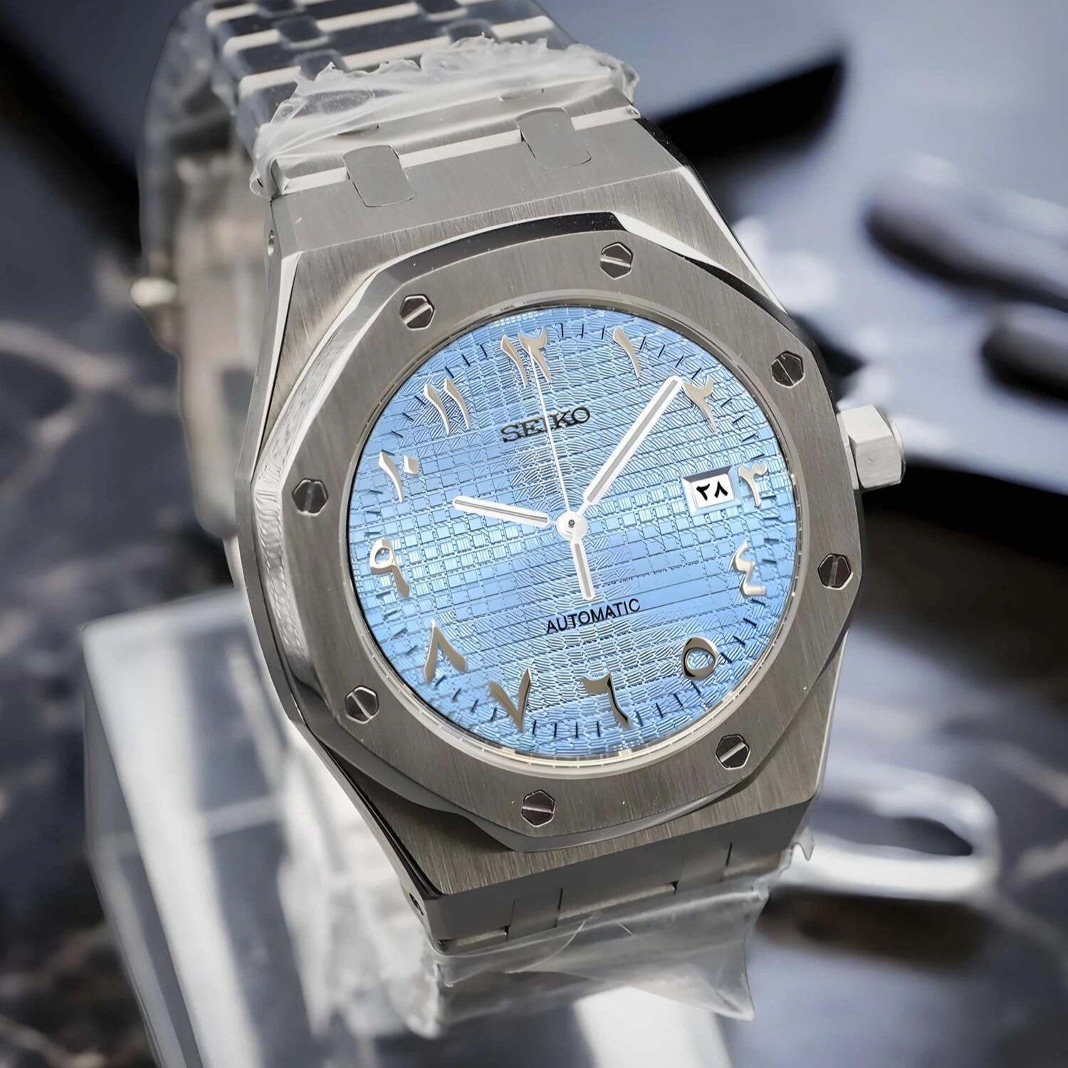 Left angled close up of Seiko Mod Royal Oak in stainless steel, ice blue textured Arabic dial, automatic movement, and polished case edge