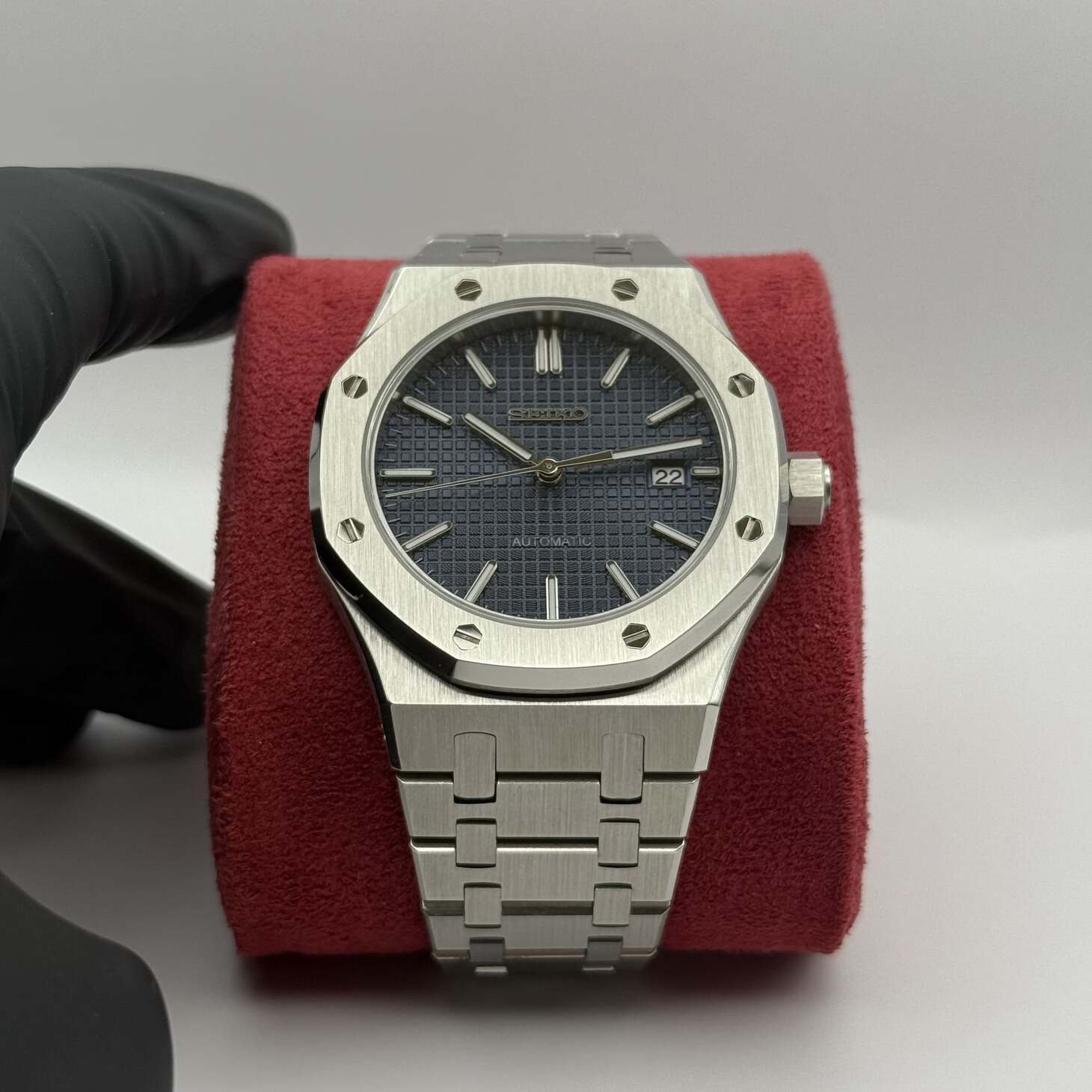 Front display of the Seiko Mod Royal Oak automatic watch with dark blue grid pattern dial, stainless steel bracelet, and date window at 3 o’clock on a red cushion