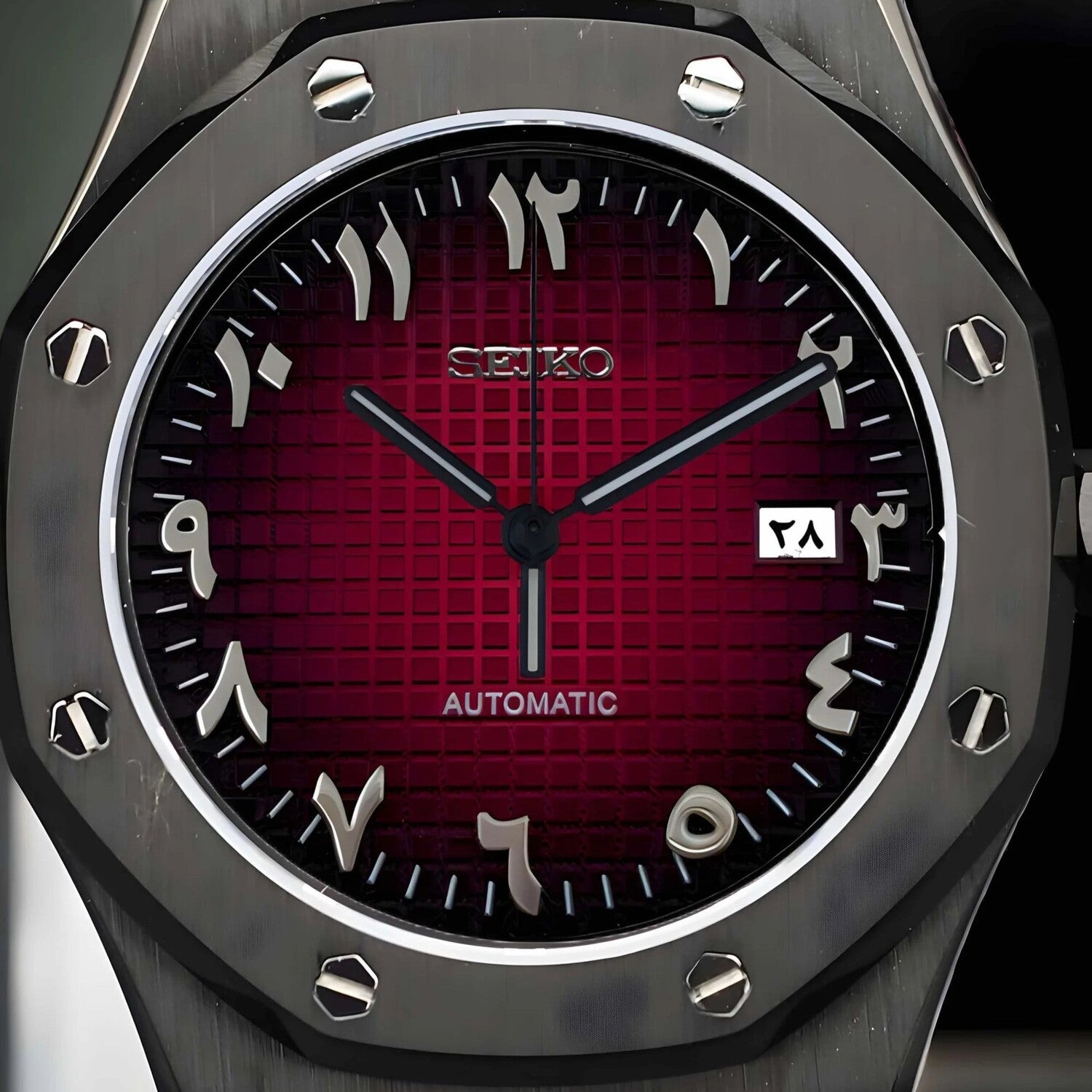Close up view of a Seiko Mod Royal Oak watch showcasing a deep red grid pattern dial with silver Arabic numerals, bold hands, and a black brushed octagonal bezel with exposed screws.