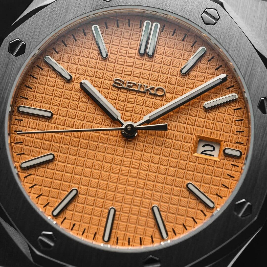 ChatGPT:
Close up of the Seiko Mod Royal Oak dial in salmon color, featuring a textured waffle pattern, applied silver tone indices, brushed octagonal bezel with exposed screws, and a framed date window at 3 o’clock.
