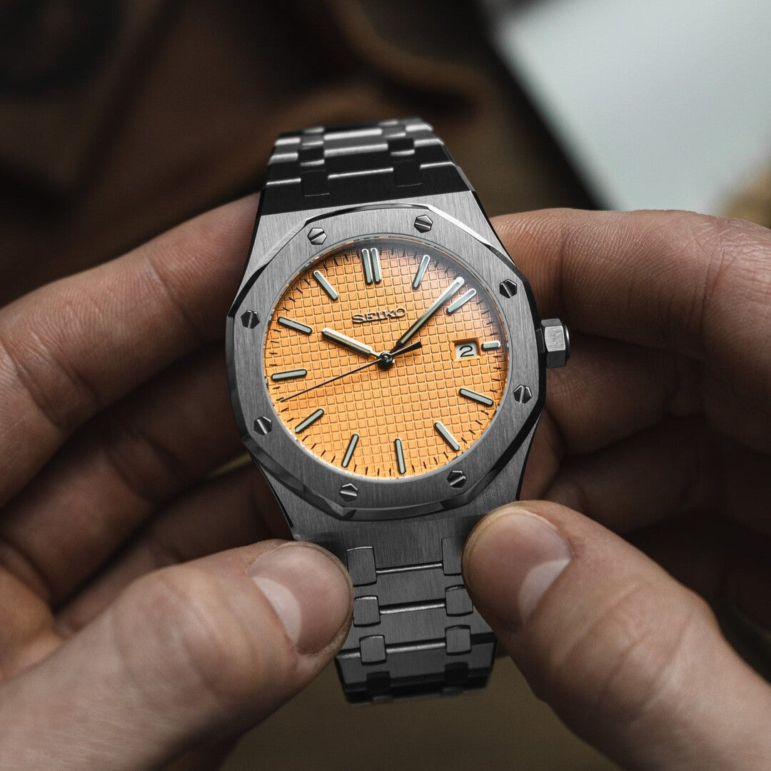 Front view of the Seiko Mod Royal Oak held in hand, showcasing a salmon colored textured dial with applied indices, brushed octagonal steel bezel with screws, and integrated stainless steel bracelet.