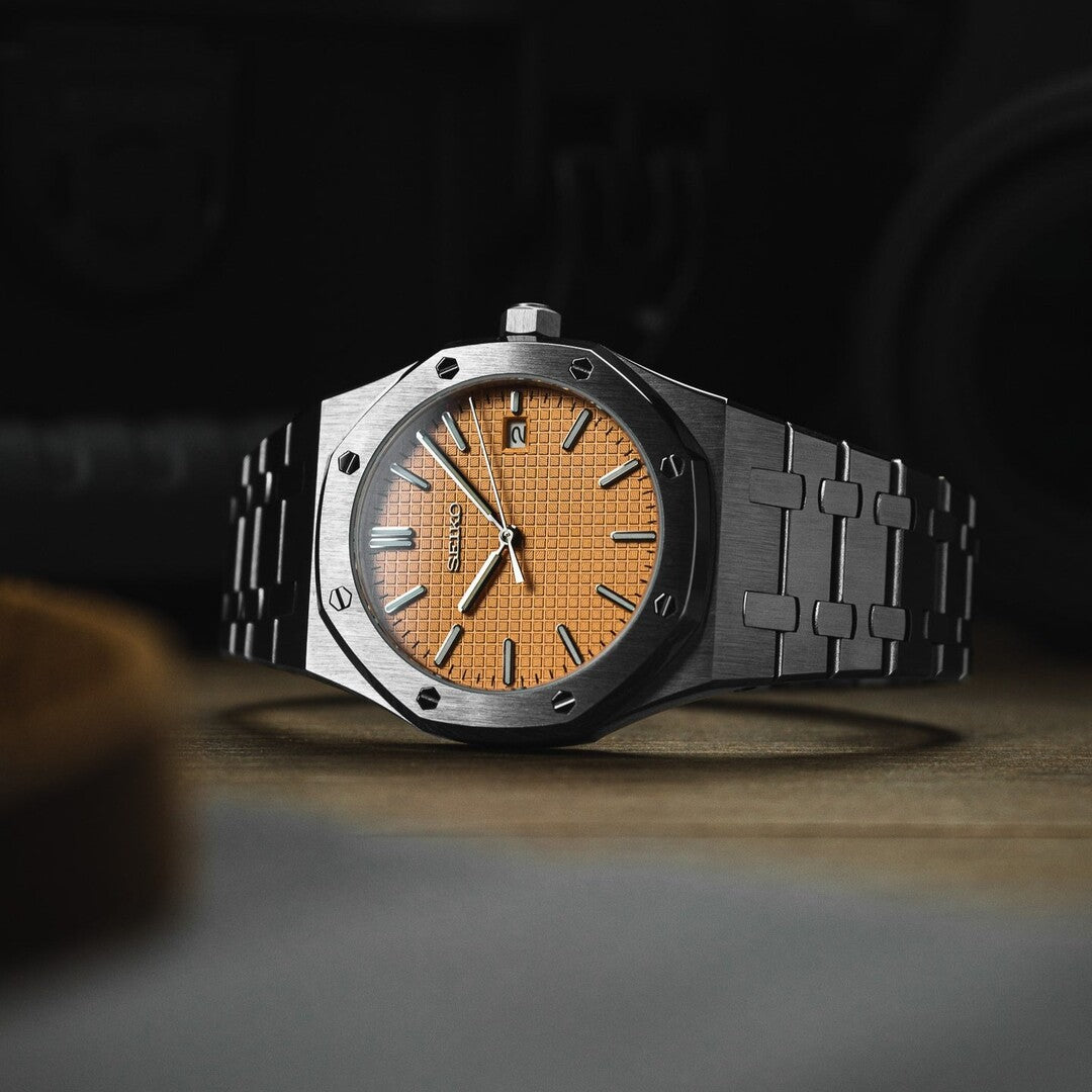 Horizontal view of the Seiko Mod Royal Oak featuring a salmon toned textured dial, brushed octagonal steel bezel with exposed screws, and integrated stainless steel bracelet on a wooden surface.