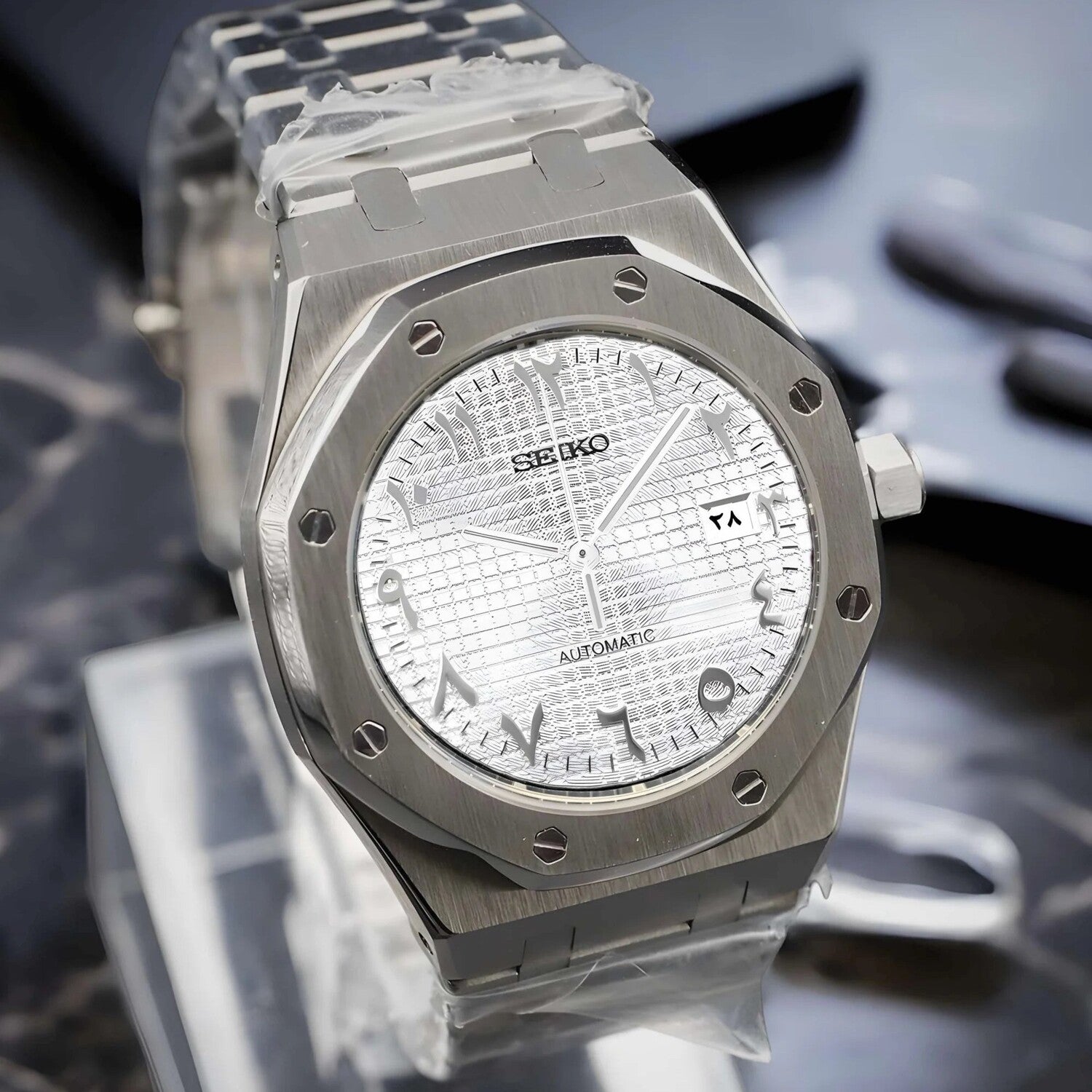 Seiko Mod Royal Oak with brushed stainless steel case shown from a left angled view, featuring a white textured dial with Arabic numerals and a visible date window.