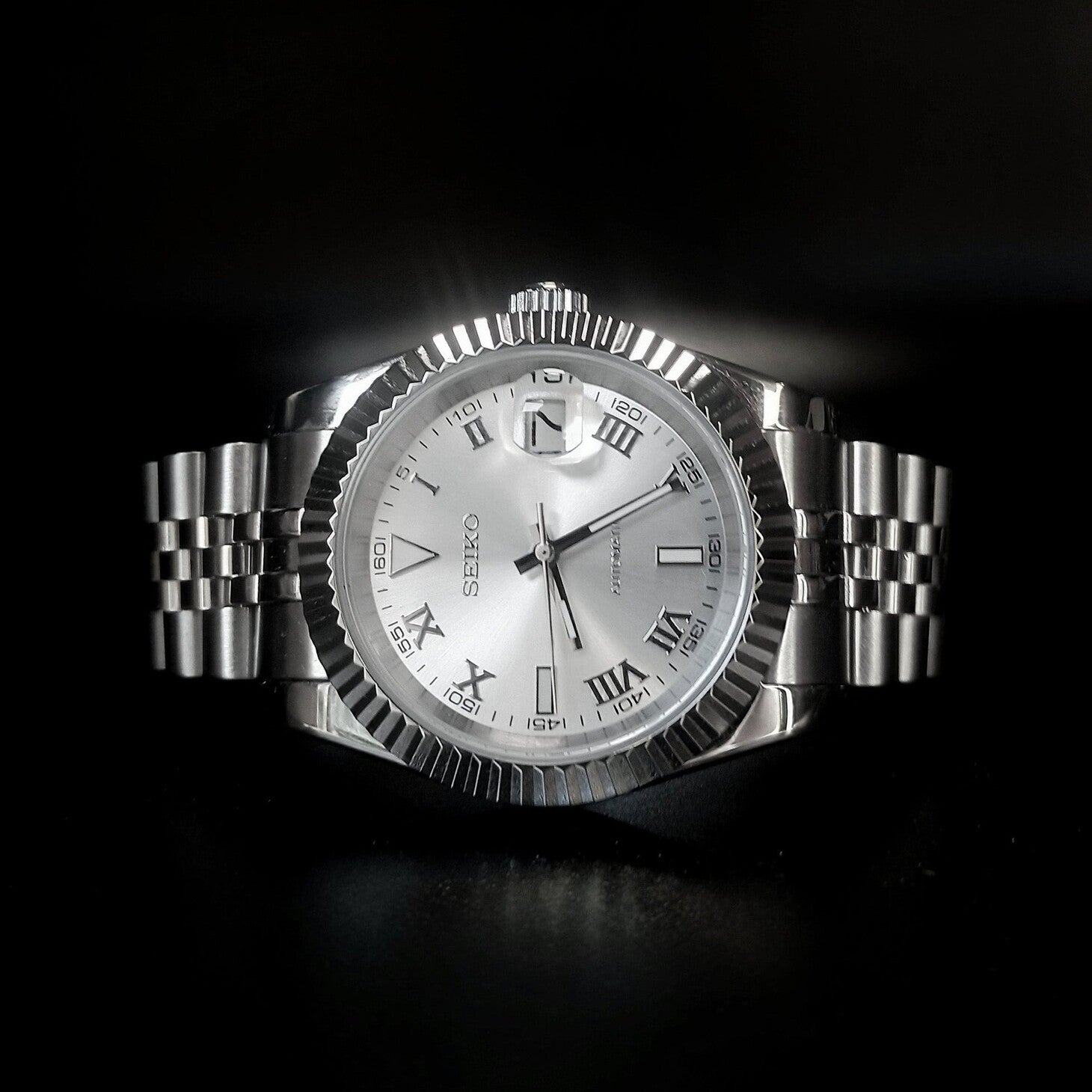 Horizontal shot showing Seiko Mod Datejust silver Roman dial under soft light