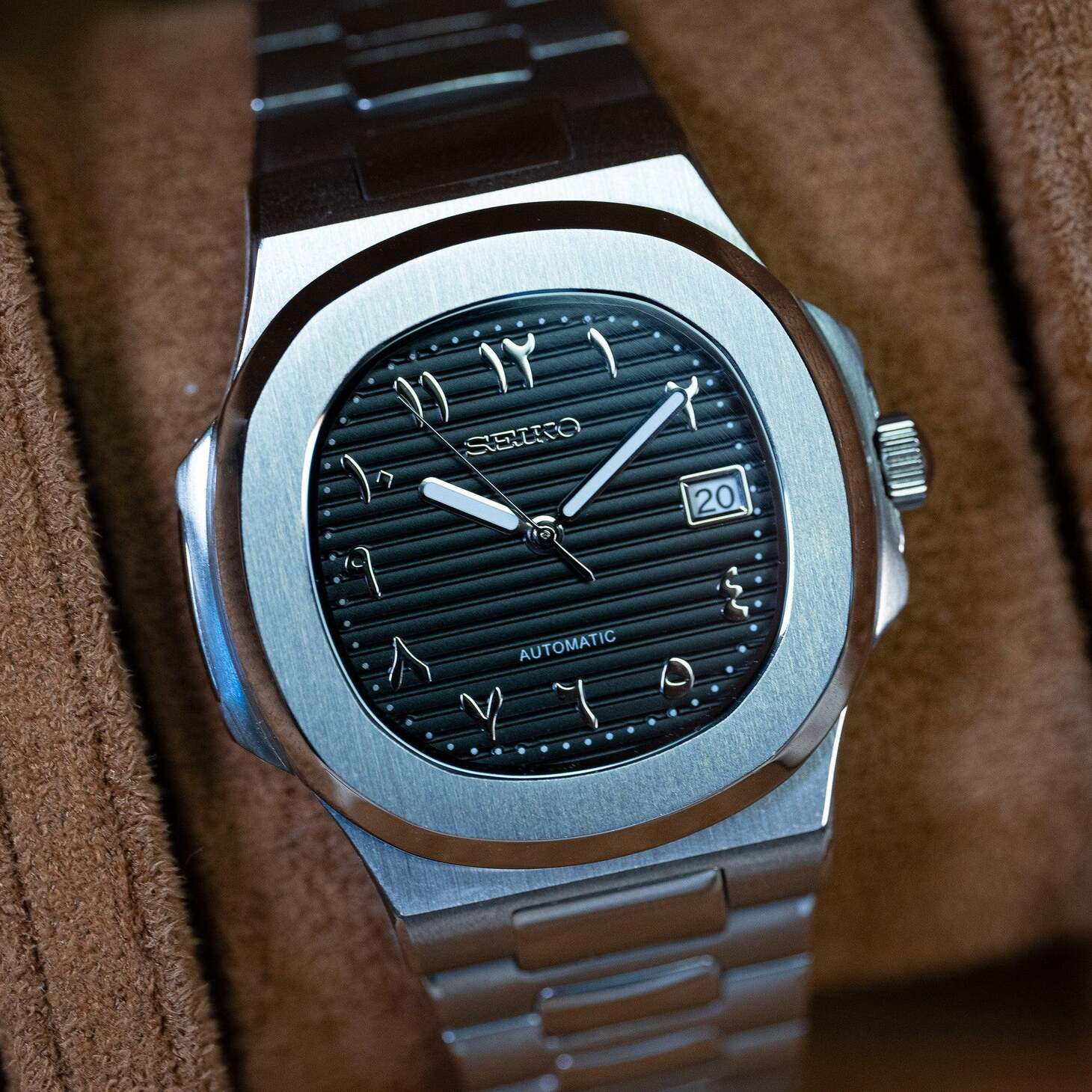 Seiko mod Nautilus black Arabic dial close up with brushed bezel on suede background