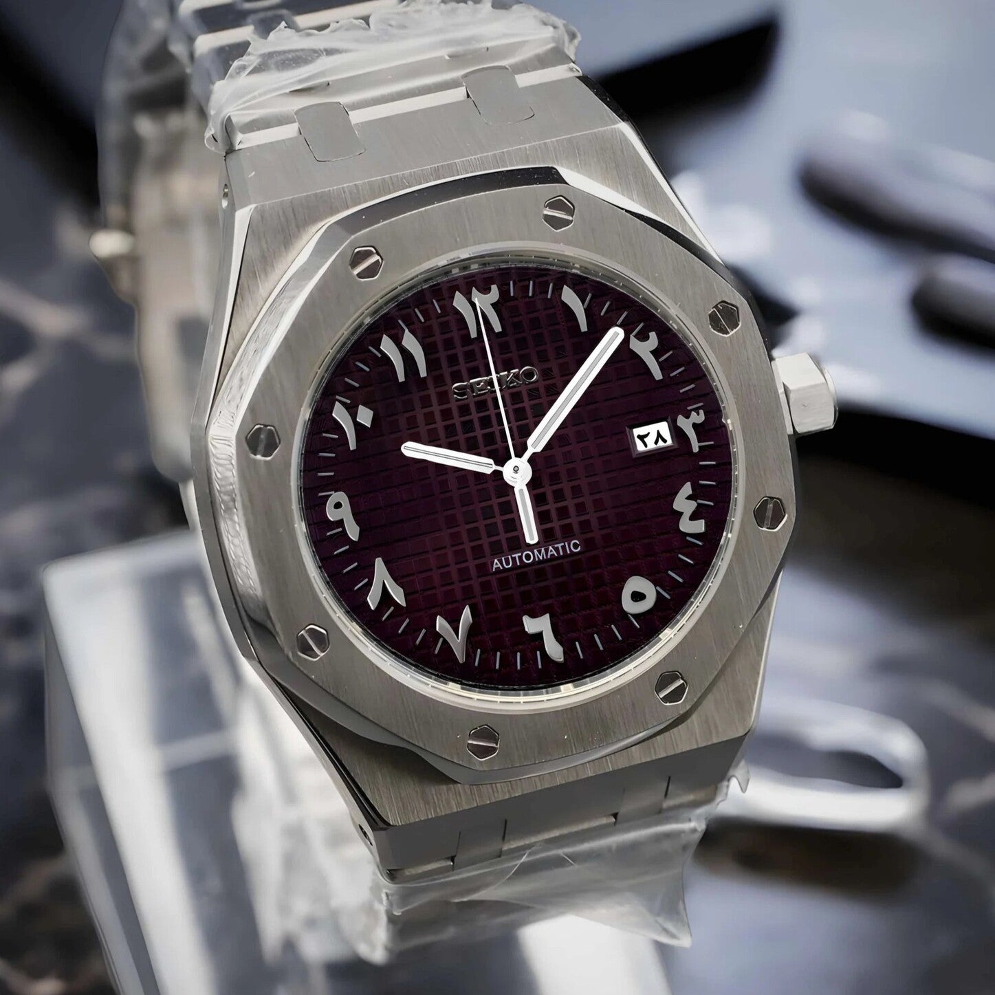 Left angle view of the Seiko Mod Royal Oak with brushed stainless steel case, deep brown dial featuring Arabic numerals, and a silver framed date window.