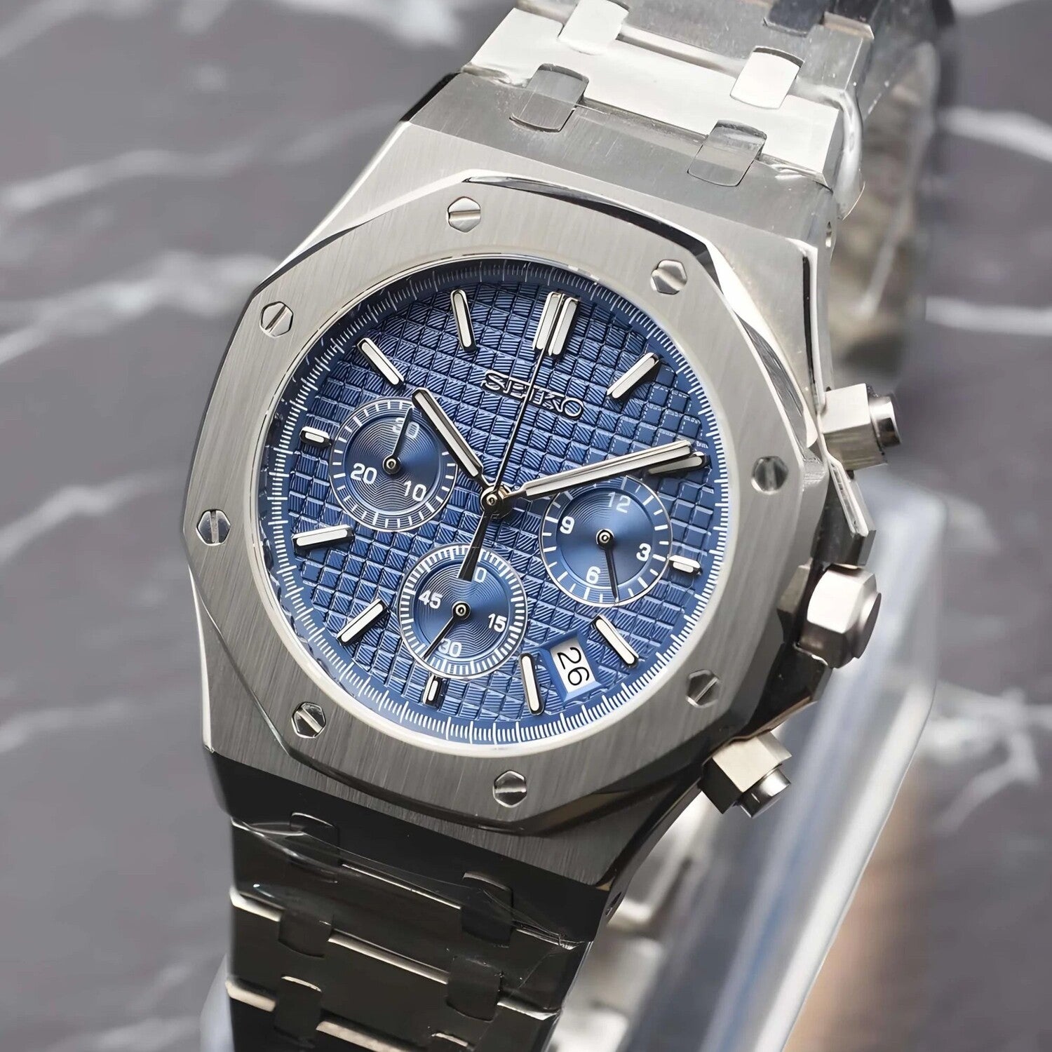 Angled close up of the Seiko Mod Royal Oak VK63 chronograph watch with blue textured dial, three functional subdials, brushed stainless steel case and bracelet, chronograph pushers, and date window between 4 and 5 o’clock