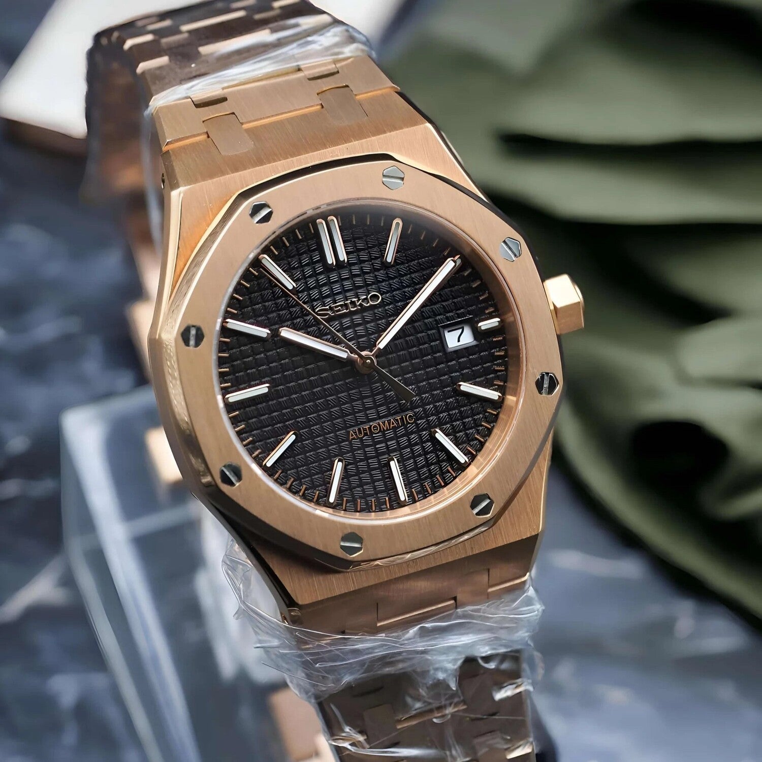 Left angled view of a Seiko Mod Royal Oak in rose gold, showcasing a textured black dial with slim luminous hour markers, date window at three o’clock, and matching rose gold hands, framed by an octagonal bezel with exposed screws and a rose gold bracelet.
